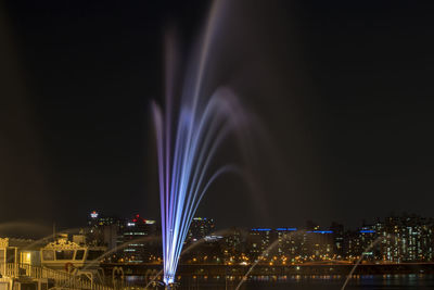 Illuminated fountain over han river by cityscape against sky