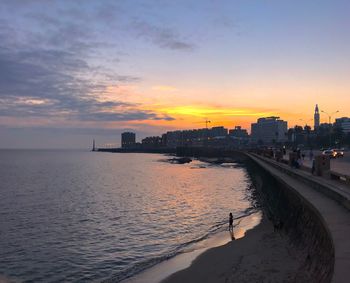 Sea and buildings against sky during sunset