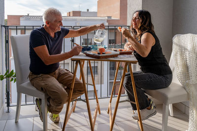 Beautiful middle aged couple eating chinese take away food sitting at a laid table in a city balcony