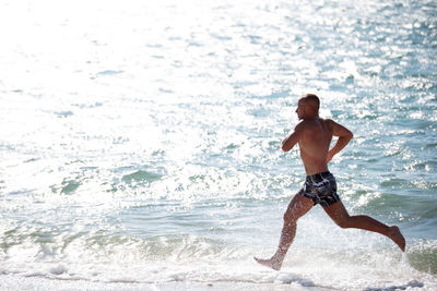 Full length of shirtless man running on shore at beach