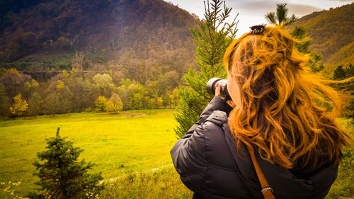 Rear view of young woman photographing mountains through digital camera