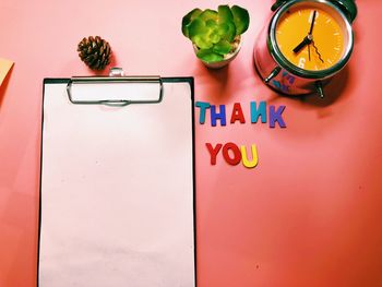 High angle view of clipboard with alarm clock and thank you sign on red background