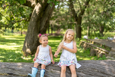 Portrait of cute girls sitting on tree trunk at park