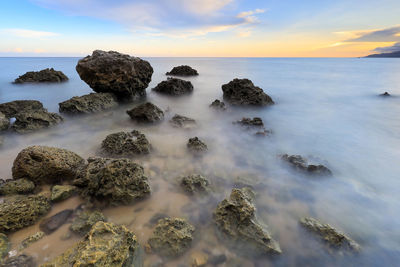 Rocks on shore against sky during sunset