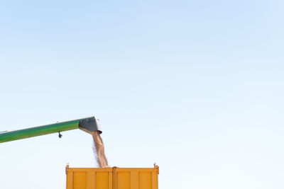 Low angle of detail of combine harvester pouring wheat grain in trailer while working in agricultural field in countryside