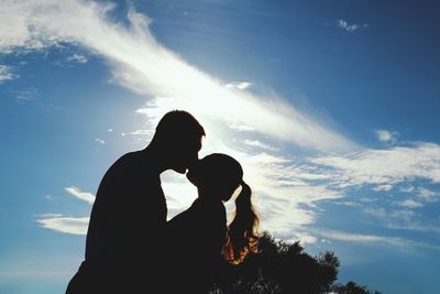 Side view of young couple kissing against sky