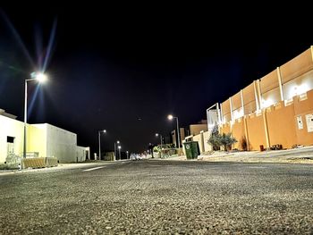 Empty road by illuminated buildings against sky at night