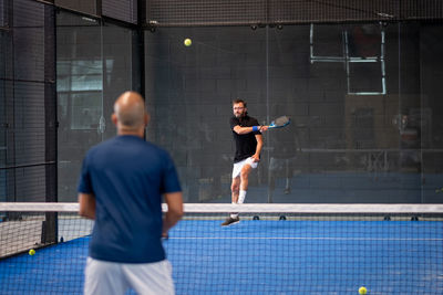 Monitor teaching padel class to man, his student - trainer teaches boy how to play padel on indoor 