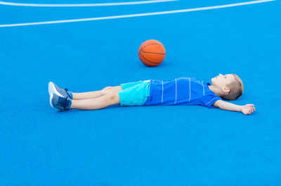 Boy lying by basketball on sports court