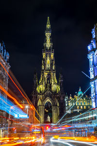 Light trails on illuminated building against sky at night