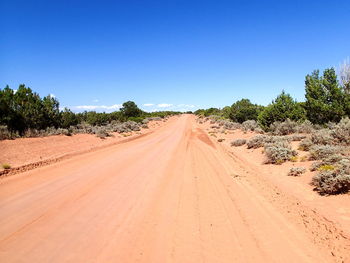 Dirt road passing through desert against clear blue sky