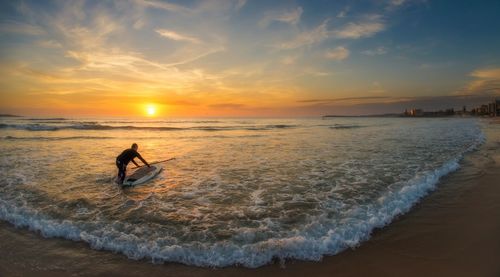 Man preparing for surfboarding on beach during sunset