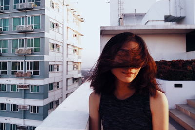 Young woman with tousled hair standing at building terrace in city