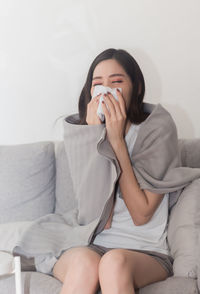 Young woman blowing nose on sofa at home