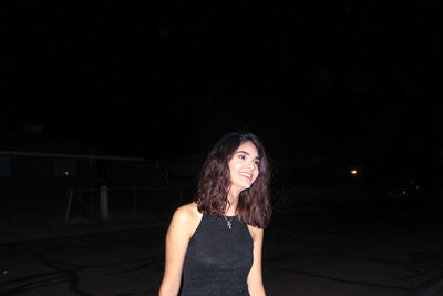 Smiling beautiful woman looking away while standing against sky at night