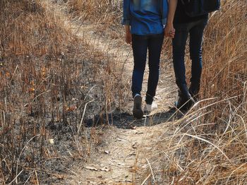 Low section of couple holding hands while walking on grassy field