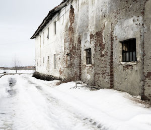 Snow covered road by buildings against sky