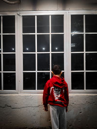 Rear view of man standing by window against building at night