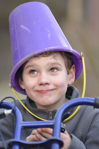 Close-up of boy with bucket on head riding bicycle