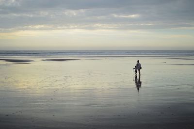 Man walking on beach against sky during sunset