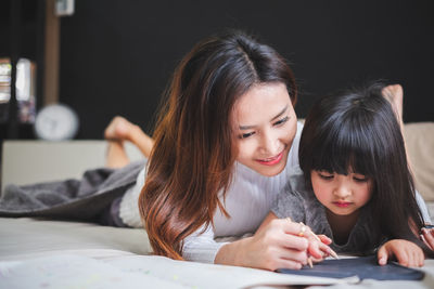 Mother assisting daughter in writing on blackboard at home