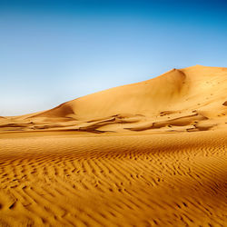 Sand dunes in desert against clear blue sky