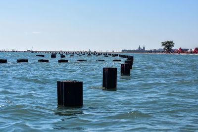 Wooden posts in sea against clear blue sky