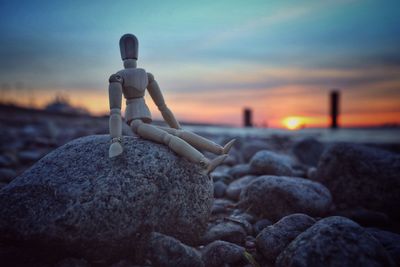 Close-up of wooden figurine on rock against sky during sunset