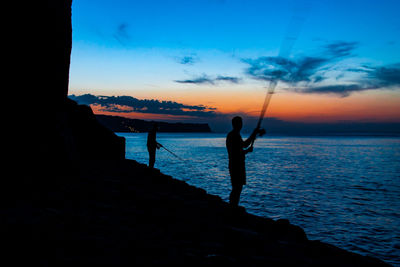 Silhouette man fishing on beach against sky during sunset