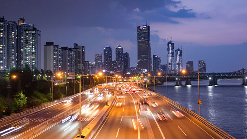 Illuminated city by buildings against sky at night