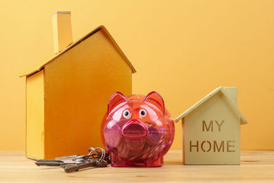 Close-up of piggy bank with model homes on table against yellow background