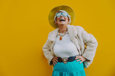 Cheerful senior woman standing against yellow background
