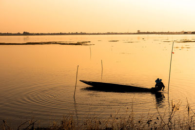 Silhouette man fishing in lake against sky during sunset