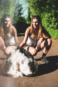 Digital composite image of woman touching dog reflecting in glass while crouching on footpath