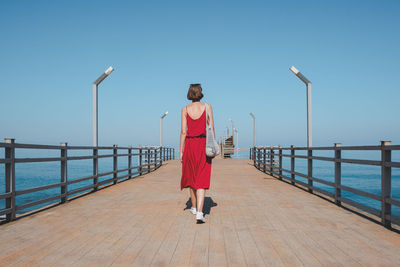 Rear view of woman standing on pier against clear sky