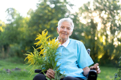 Portrait of smiling young man using mobile phone while sitting on field