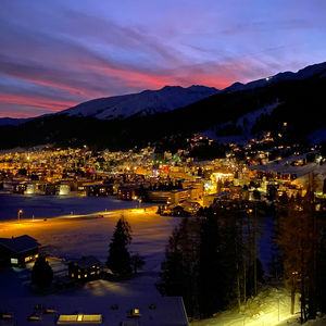 Illuminated city by mountains against sky at sunset