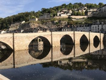 Arch bridge over river by buildings against sky