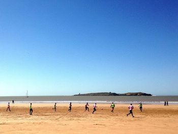 Men playing soccer at beach against clear blue sky