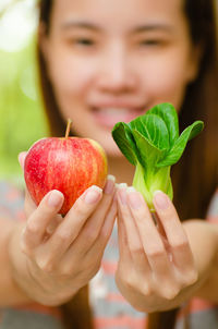 Close-up of young woman holding apple and bok choy