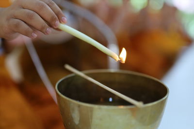 Close-up of boy lighting butter lamp with candle in temple