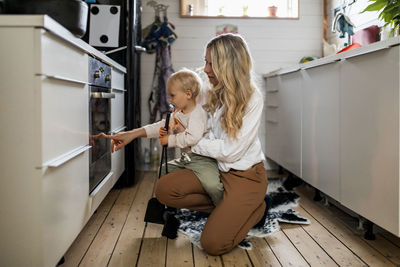 Woman showing oven to son in kitchen at home