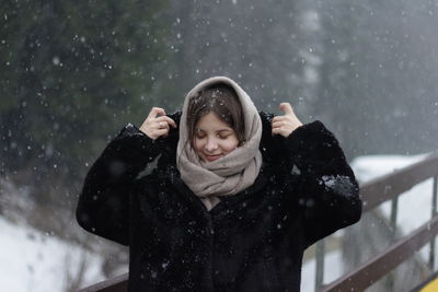 Portrait of smiling young woman standing against snow