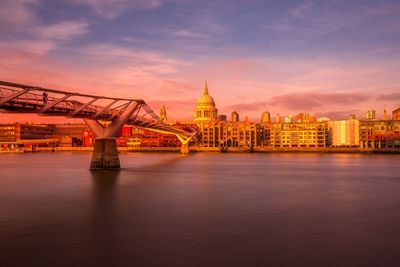 Bridge over river with buildings in background at sunset