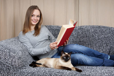 Portrait of beautiful woman with siamese cat on couch at home