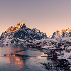 Scenic view of lake by snowcapped mountains against sky during sunset