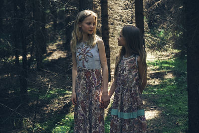 Sisters holding hands while looking at each other in forest