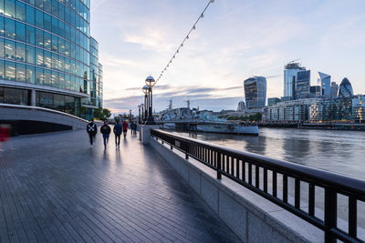 People walking by more london riverside buildings, and walkie-talkie tower in twilight.