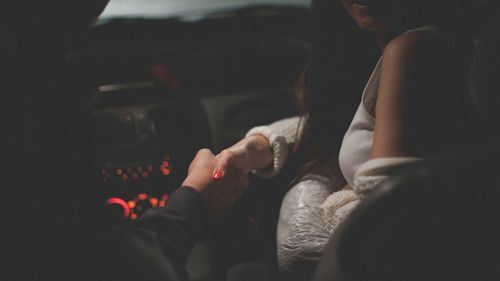 Cropped image of man holding woman hand in car