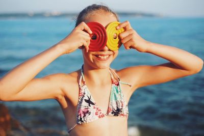 Girl in swimwear holding toys while standing at beach